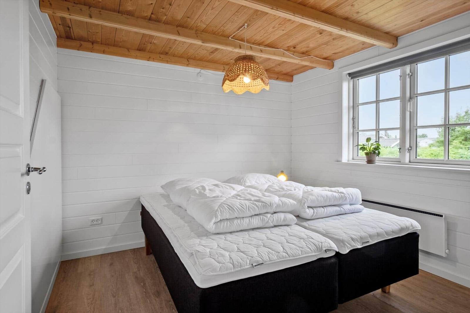Bedroom with double bed, wooden floor, and window. Ceiling with wooden beams and pendant lamp.