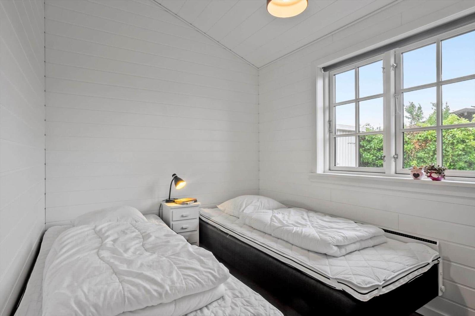 Two beds with white bedding, nightstand, and window with view of greenery.