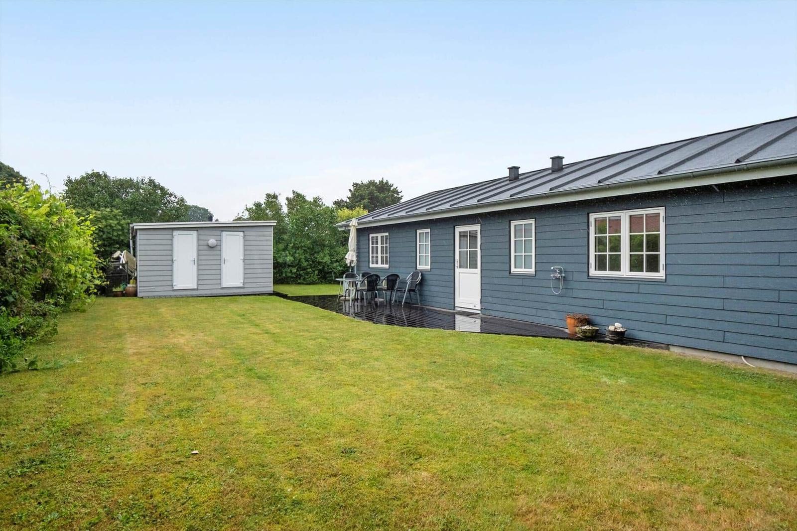 A gray house with a terrace and garden. Next to the house is a small outbuilding.