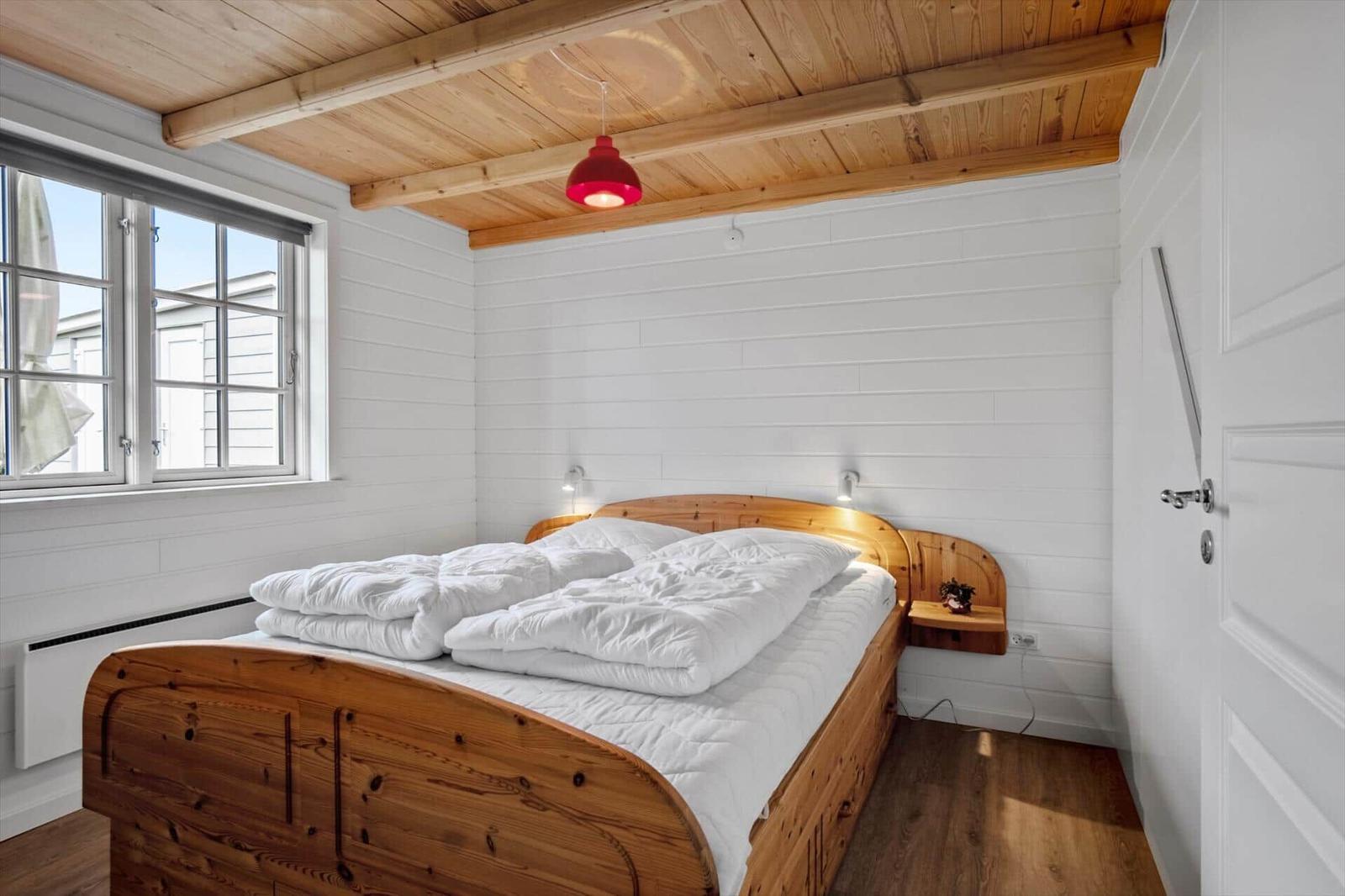 Bedroom with wooden bed, window, and ceiling beams. Red lamp hangs above the bed.