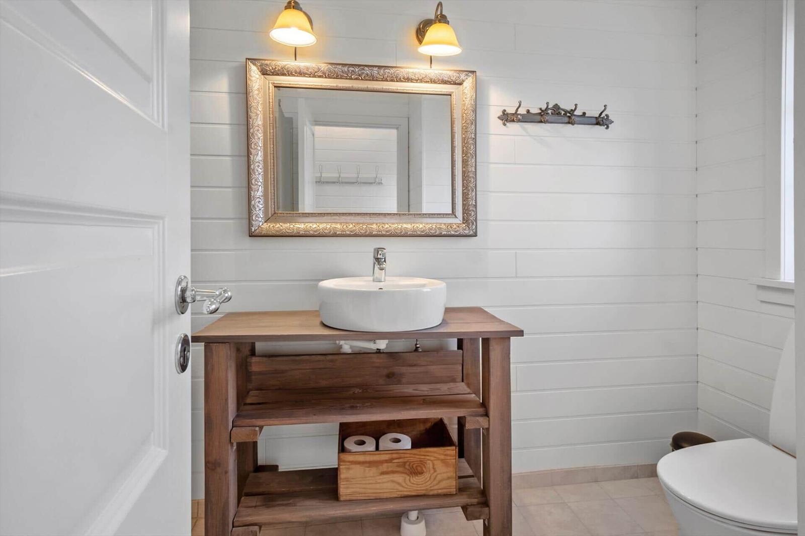 Bathroom with sink, mirror, and toilet. Wooden vanity with toilet paper box.