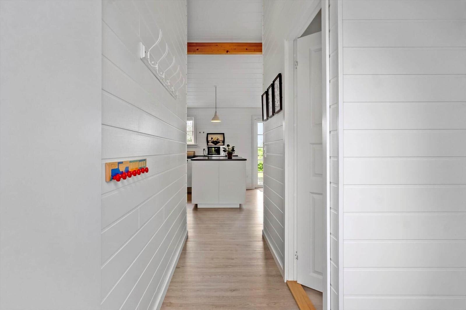 Hallway with white walls, wooden floor, and view into the kitchen.
