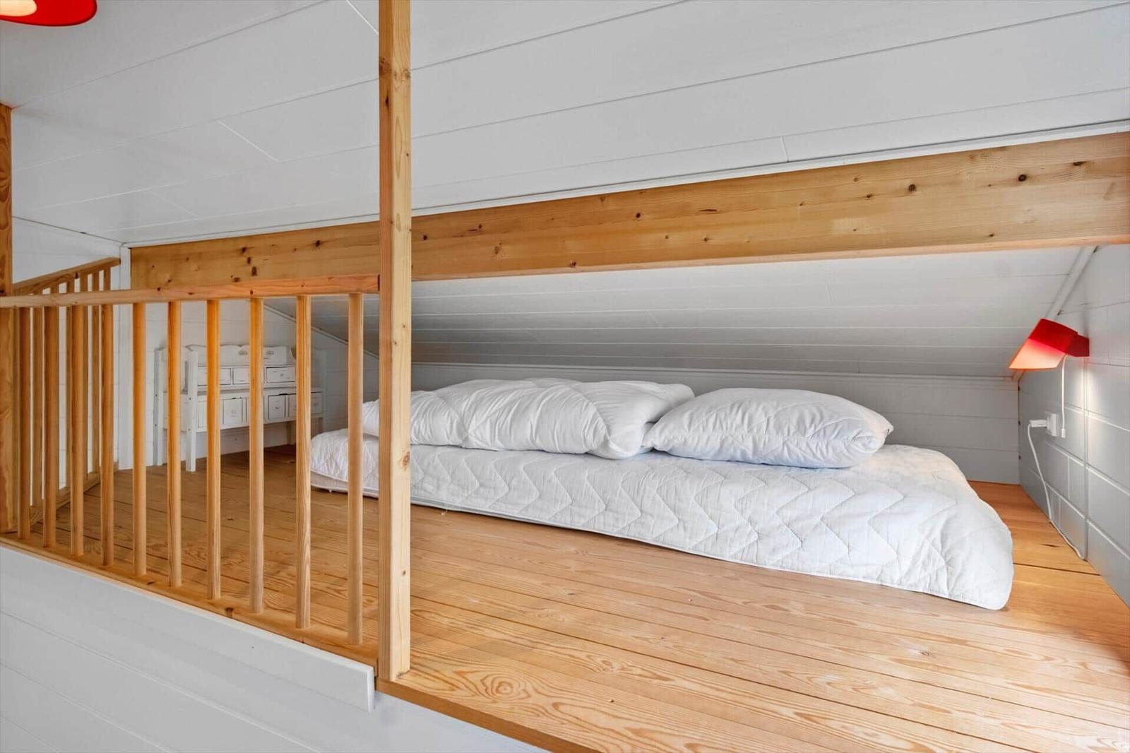 Upper level with bed and wooden railing. Lower level with cabinet and wooden floor.