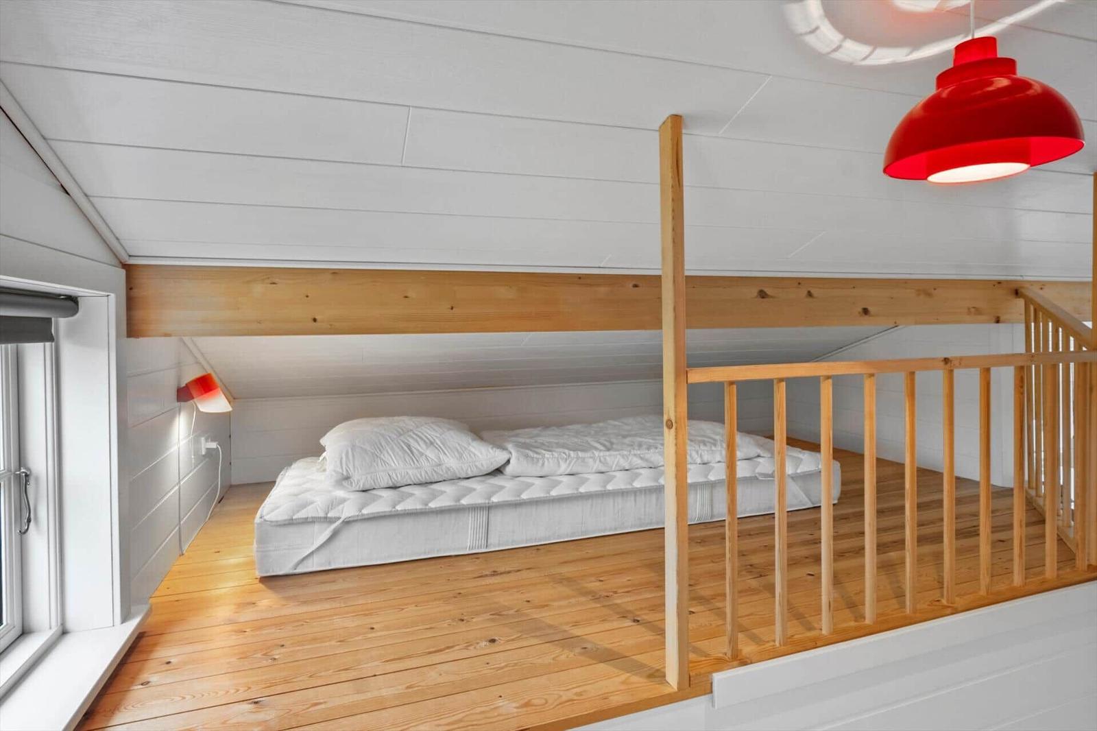 A bedroom with a double bed on a wooden platform under a sloped ceiling.