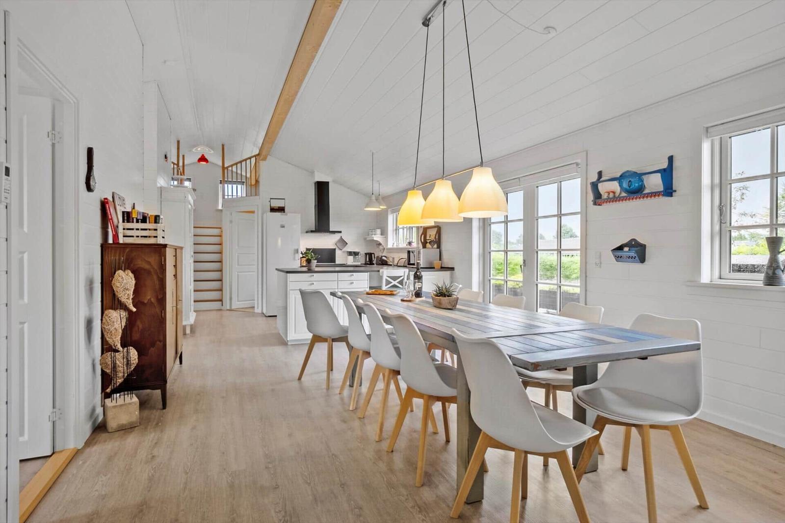 Dining area with long table and chairs. Kitchen and living area in the background.