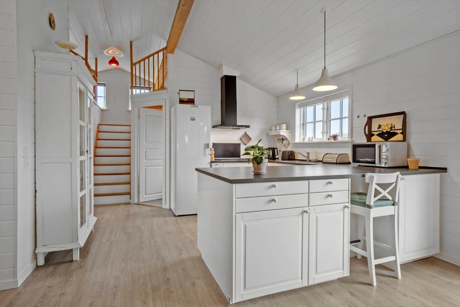 Kitchen with island, white cabinets, and hardwood floors. Background: stairs and white cabinet.