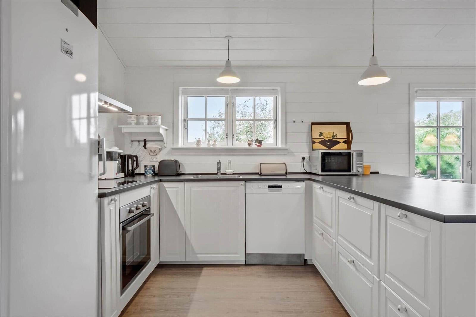Kitchen with white cabinets, dark countertop, and windows with view outside.