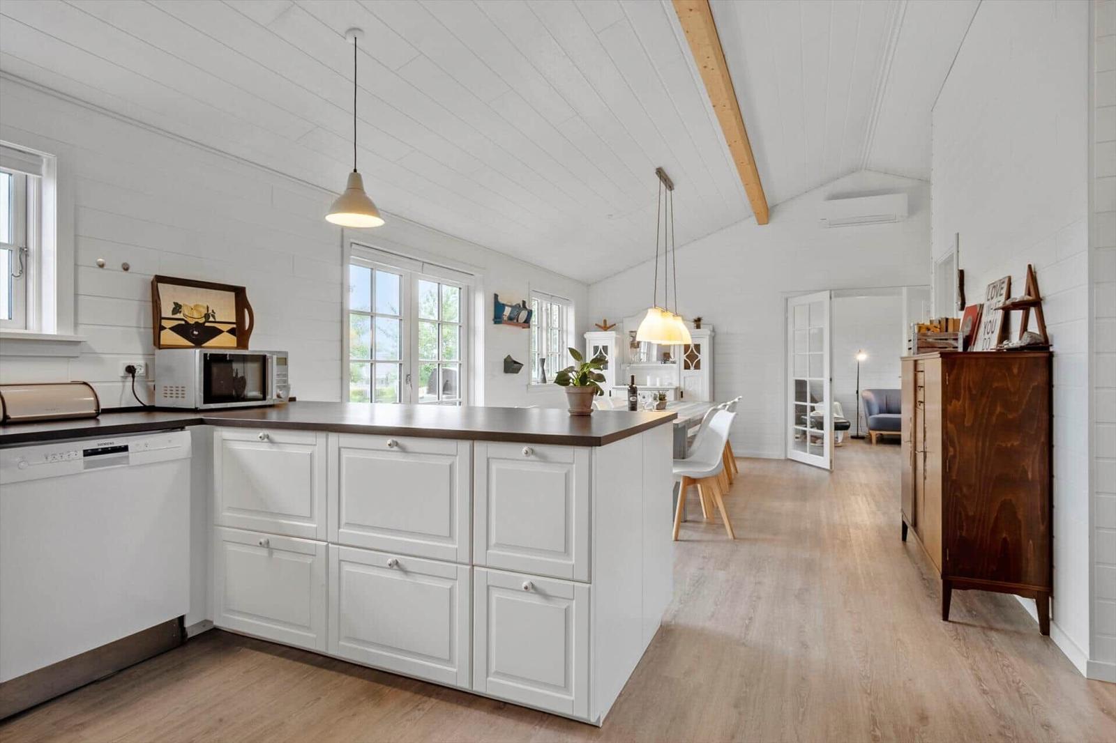 Kitchen with island, white cabinets, and wood floor. Dining area with chairs and windows.