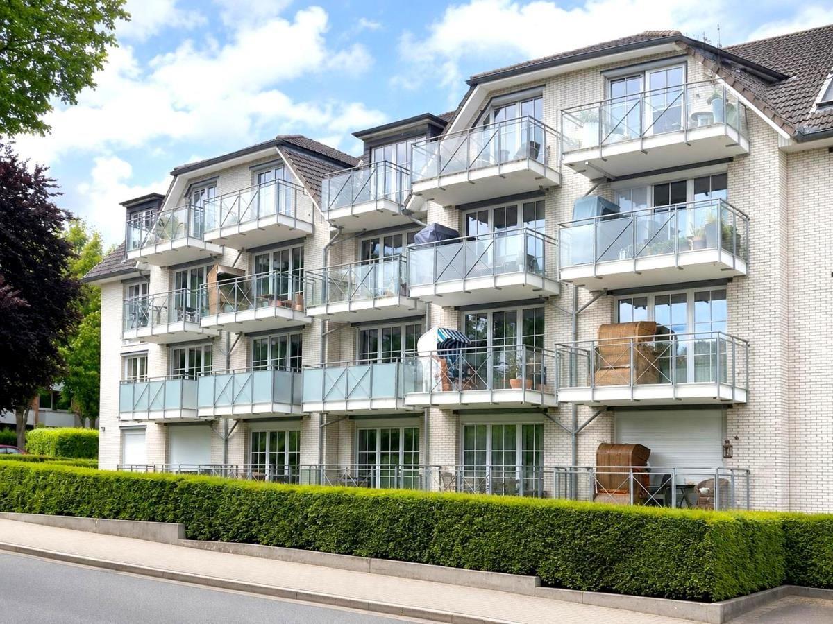 Modern apartment with balcony and glass railing, surrounded by green hedge.