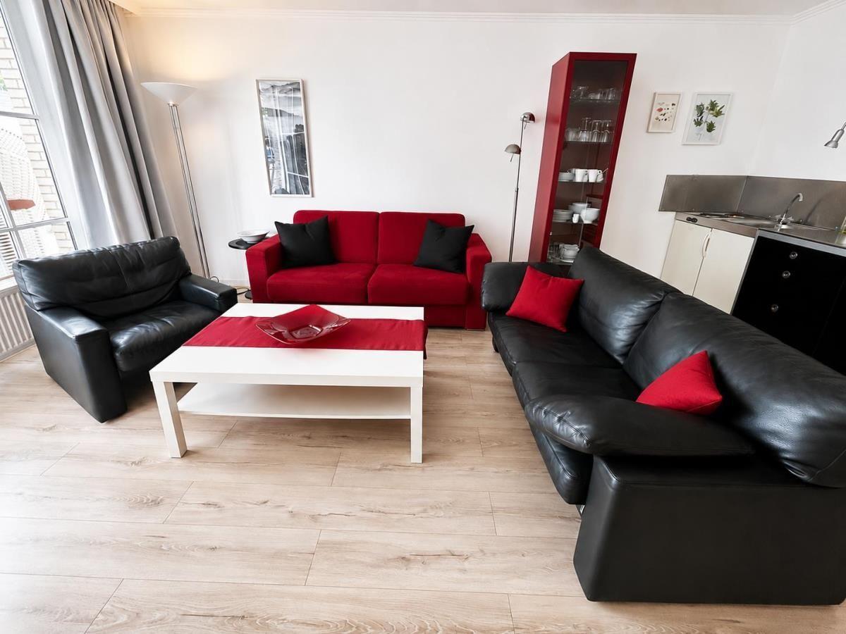 Living room with red sofa, black leather sofas, and white coffee table.