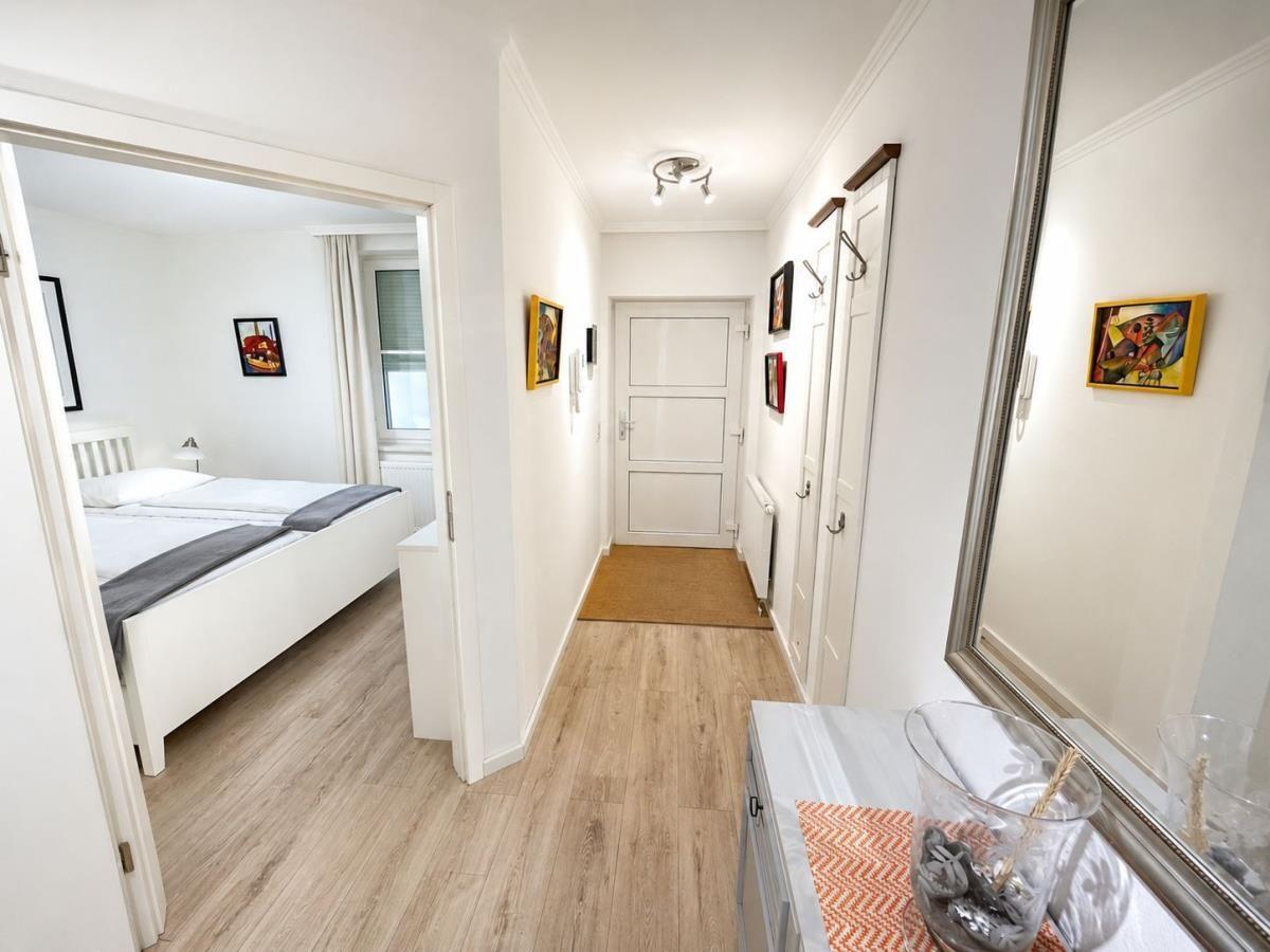 Hallway with bedroom, wall art, and mirror. Wooden floors and white walls.