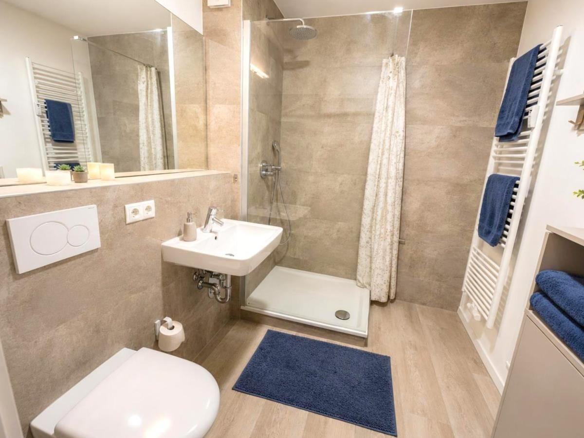 Badezimmer mit Dusche, Waschbecken und Toilette. Blaue Handtücher und Teppich.