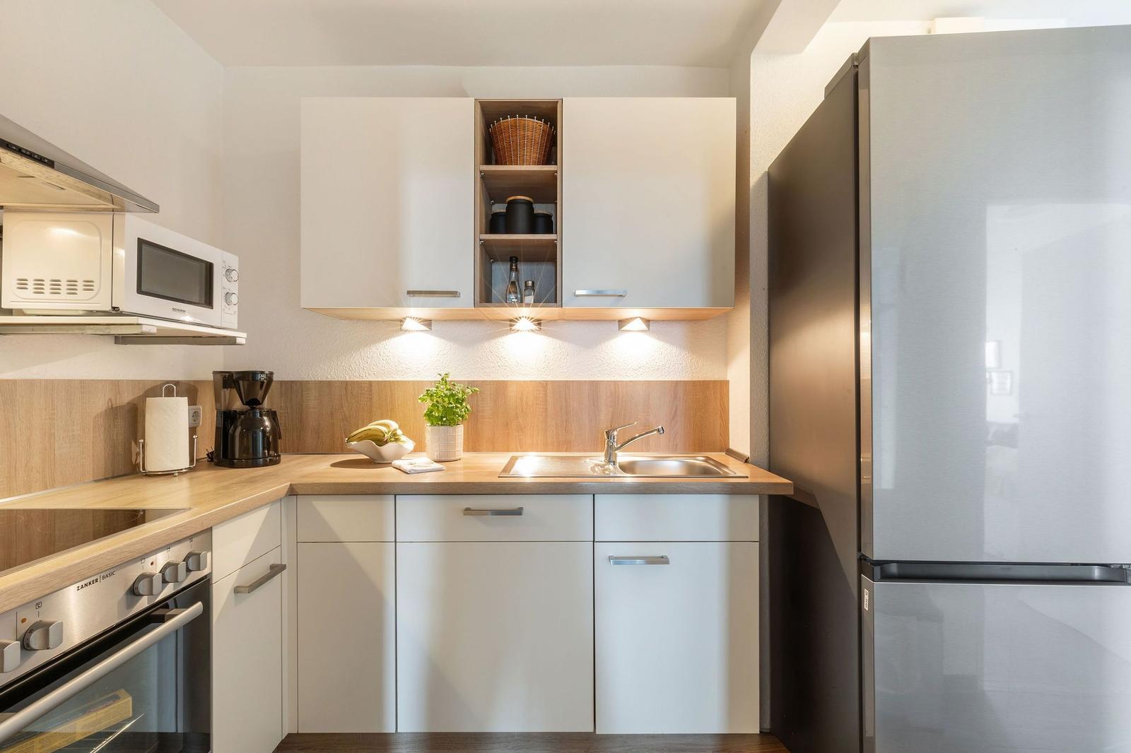 Küche mit weißen Schränken, Edelstahlspüle und Kühlschrank. Arbeitsfläche aus Holz.