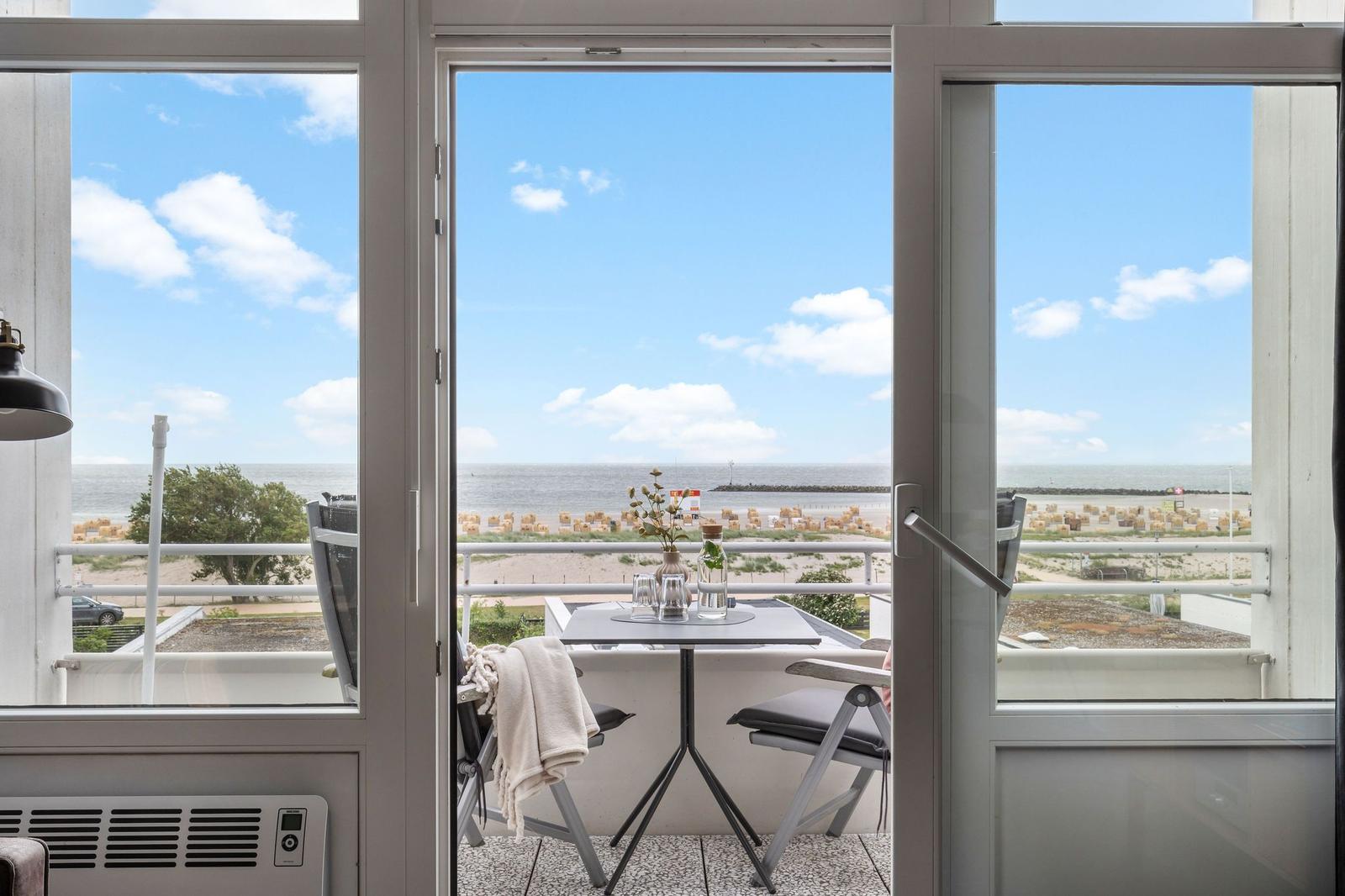Balkon mit Tisch und Stühlen bietet Blick auf Strand und Meer.