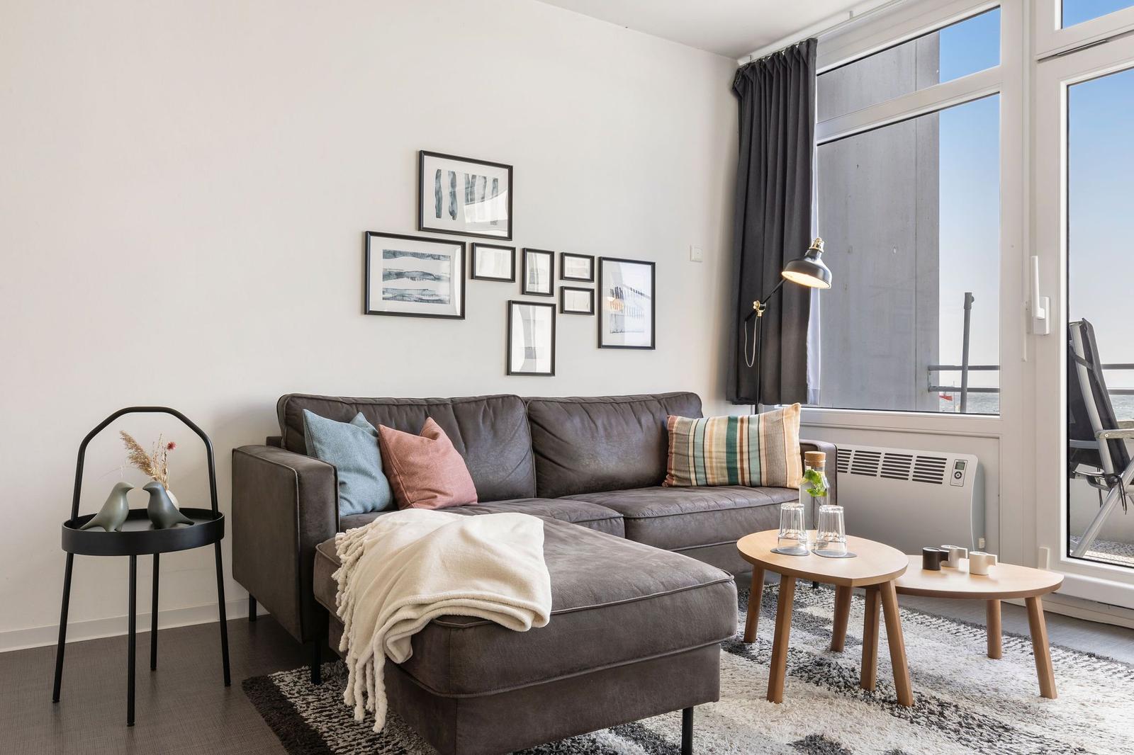 Ein Wohnzimmer mit grauem Sofa, Wandbildern und großem Fenster zur Aussicht.