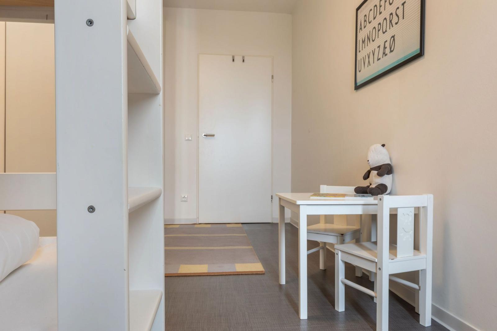Ein Kinderzimmer mit Schreibtisch, Stuhl und Plüschtier. An der Wand hängt ein Alphabetbild.