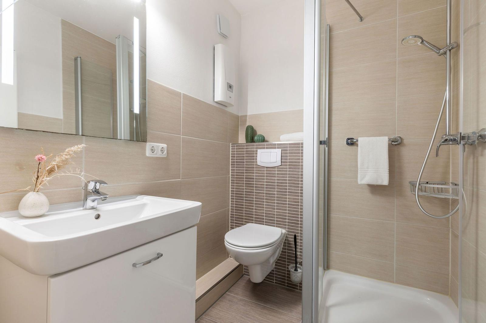 Bad mit Dusche, Waschbecken und WC. Fliesenwand und Spiegel.