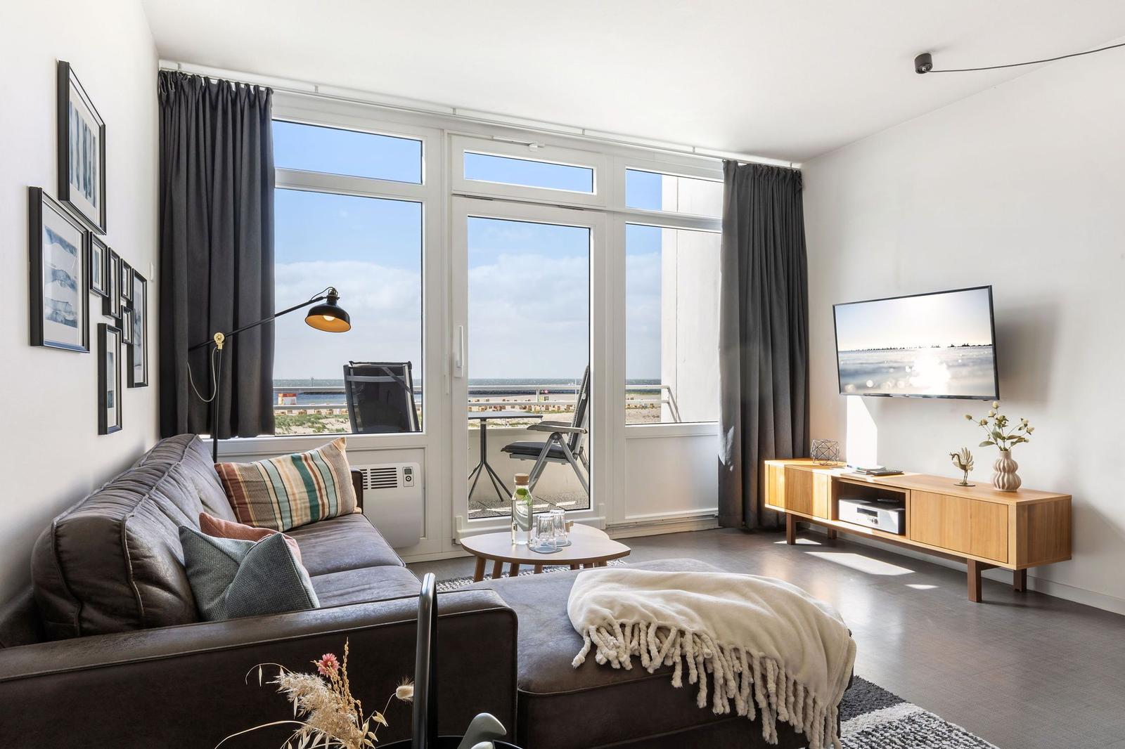 Wohnzimmer mit Sofa, Fernseher und Balkonblick