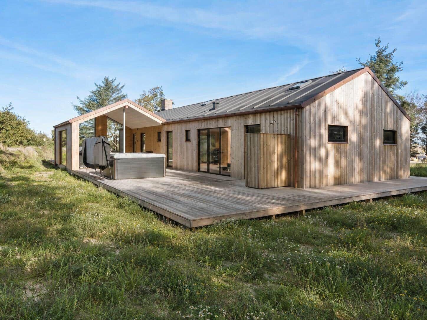 Moderne Holzhütte mit Terrasse und Whirlpool in grüner Umgebung.