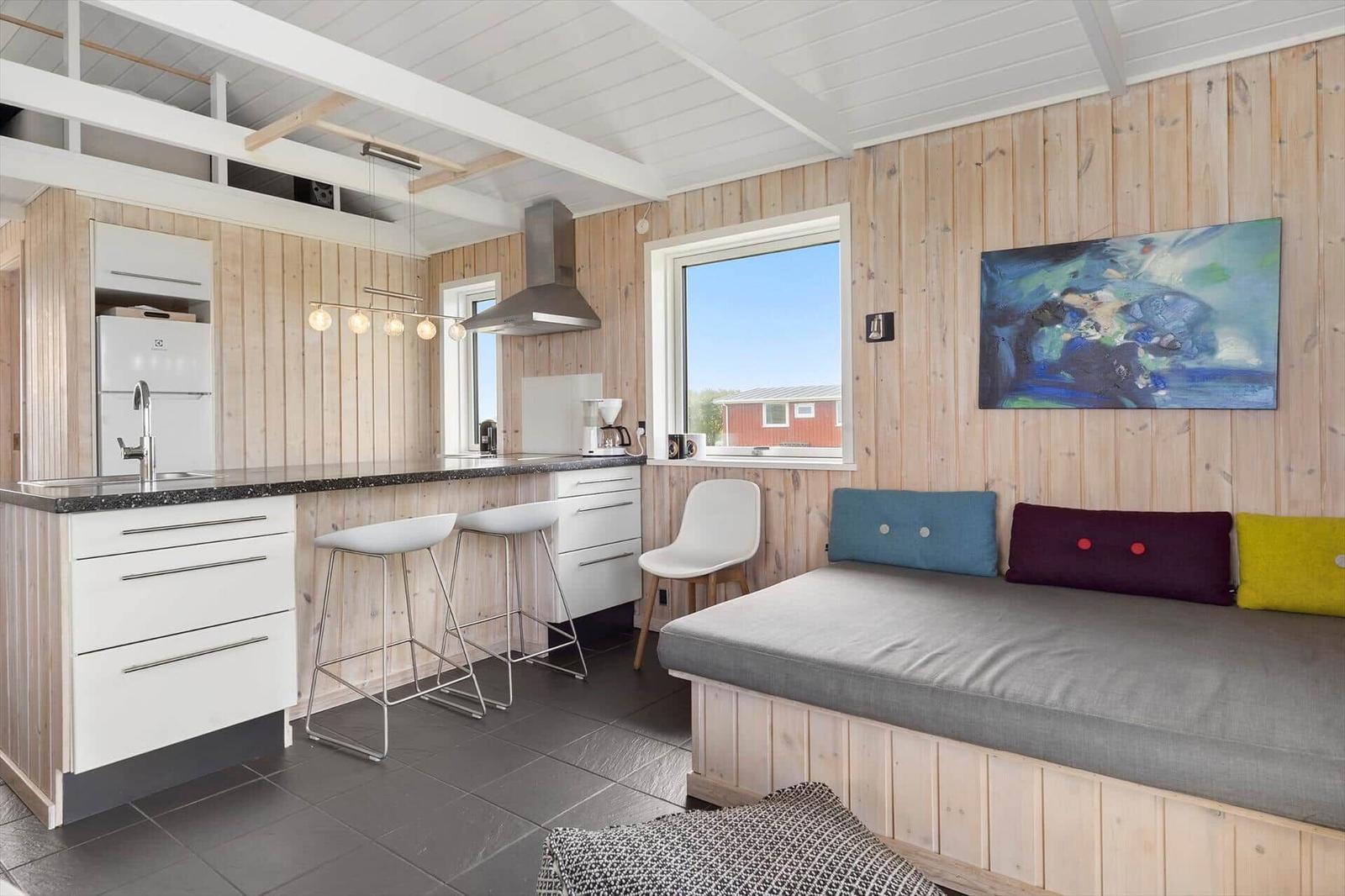 Küche mit Arbeitsplatte, Barhocker und Fenster. Sofa mit Kissen und Wandbild.