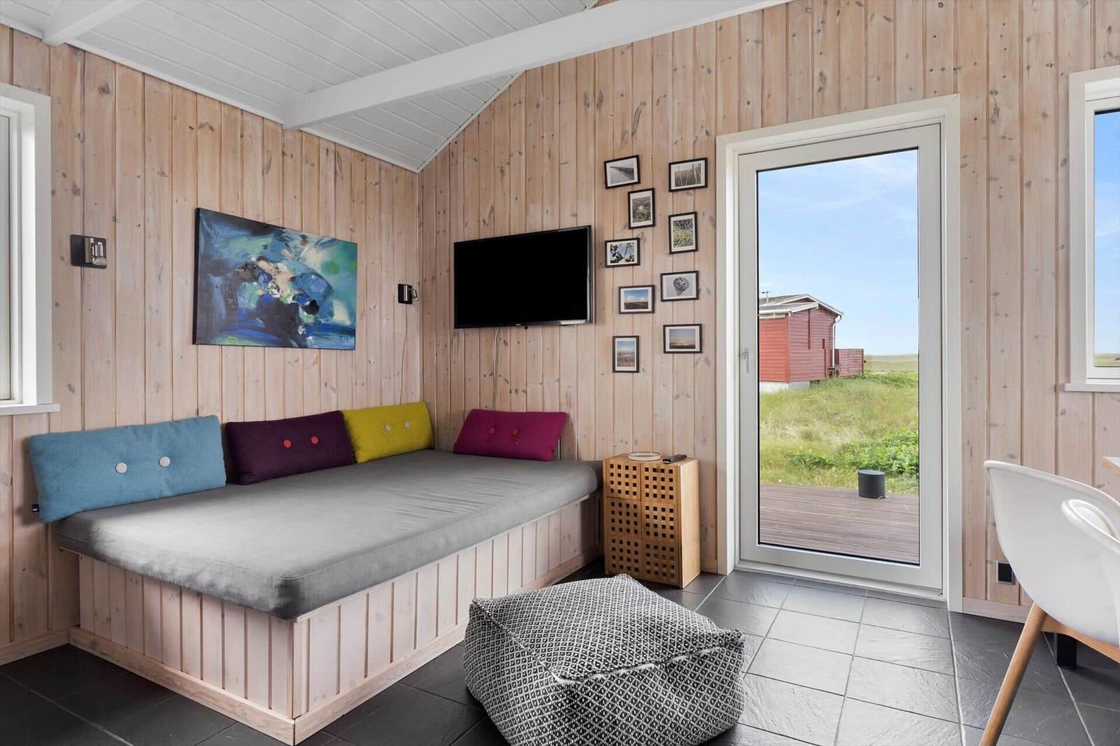 Ein Raum mit Holzwand, Sofa, Fernseher und Blick auf eine Terrasse.