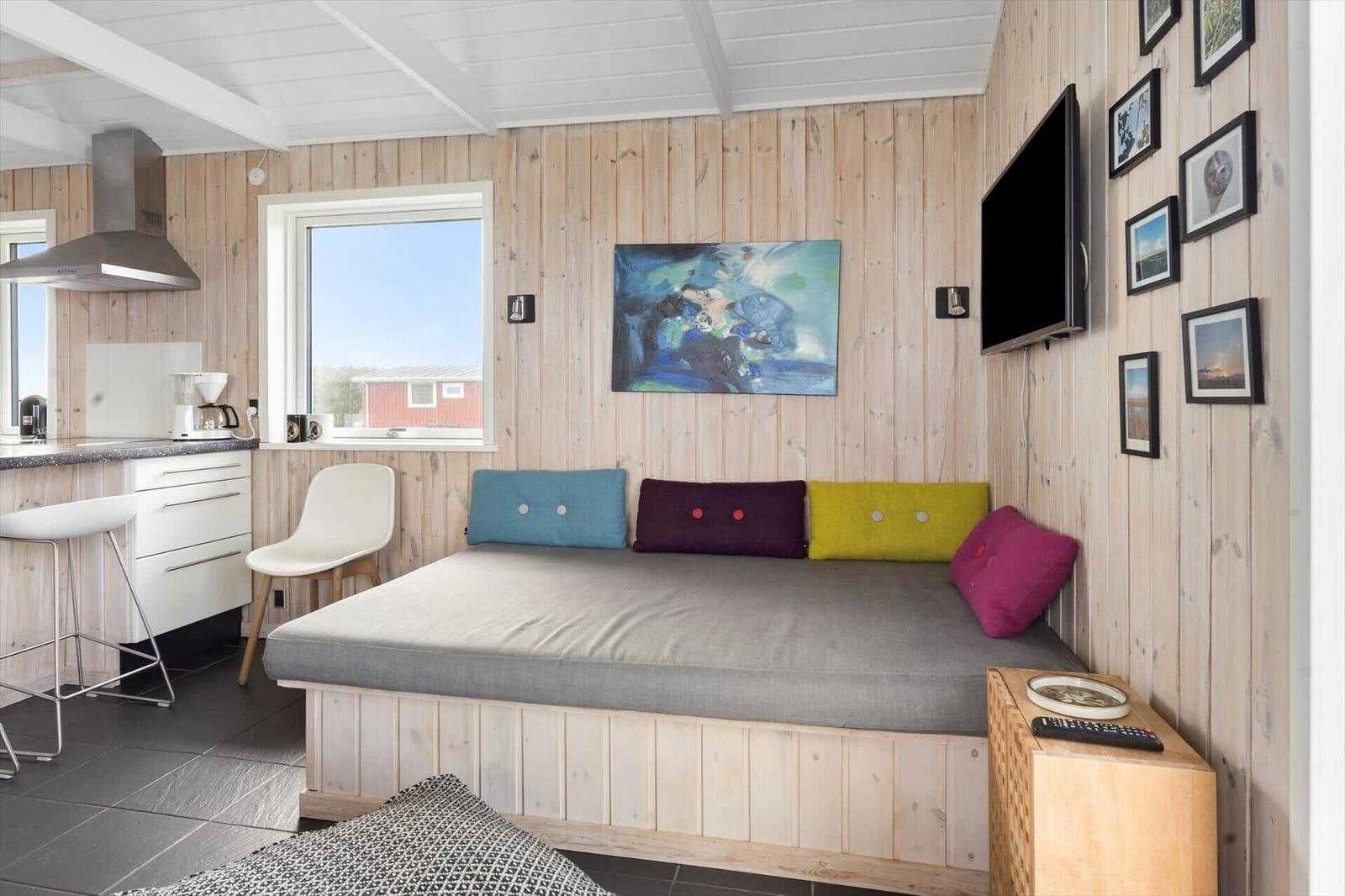 Ein Raum mit Holzwänden, einem Bett mit bunten Kissen und einer Küchenzeile.