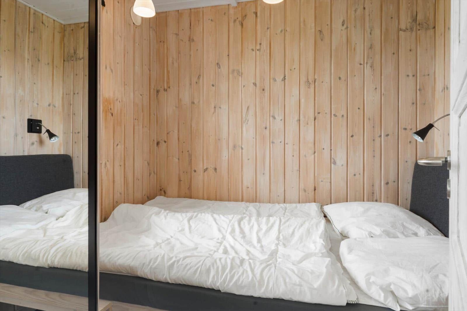 Schlafzimmer mit Holzwand und Bett mit weißer Bettwäsche.