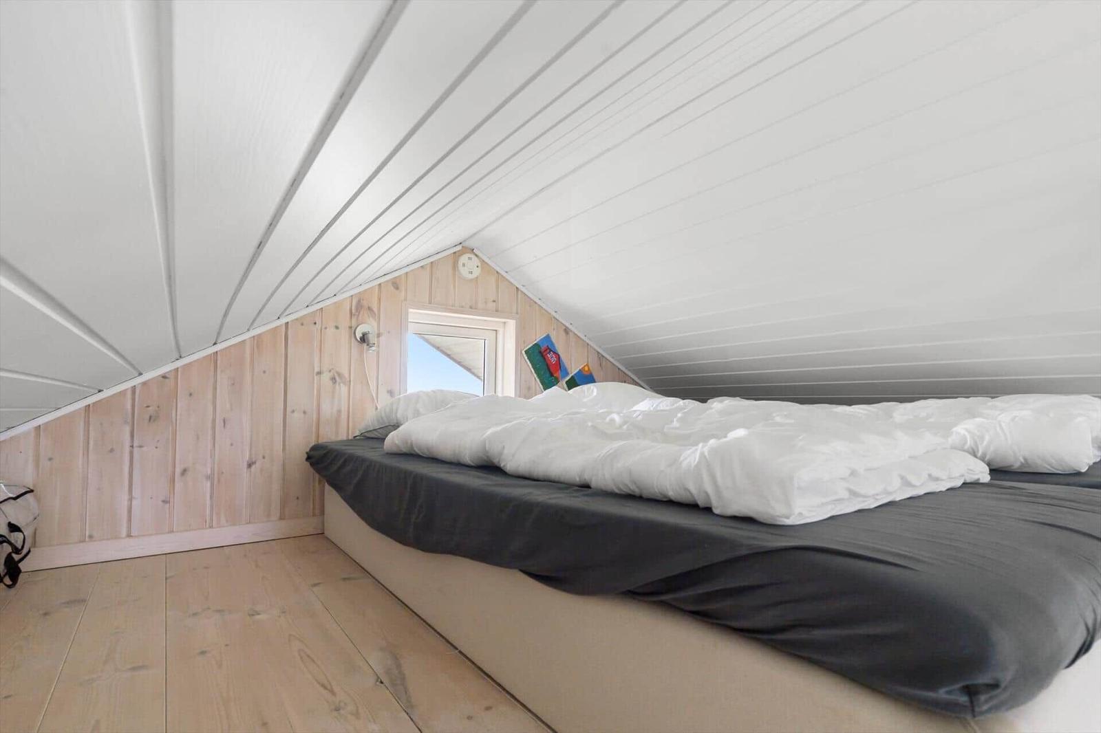 Schlafzimmer mit Dachschrägen, Holzwand und Bett mit weißer Bettwäsche.