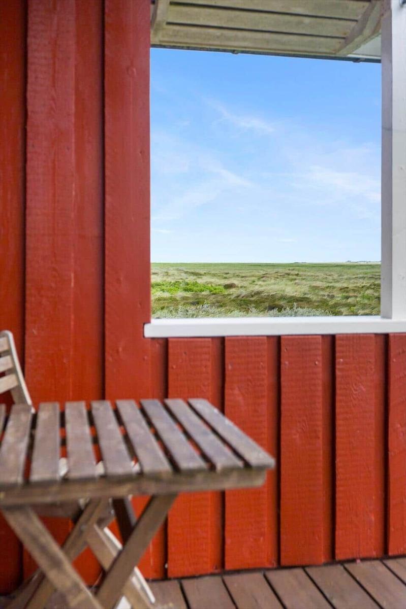 Roter Holzaufbau mit Tisch und Stuhl. Blick auf grünes Feld unter blauem Himmel.