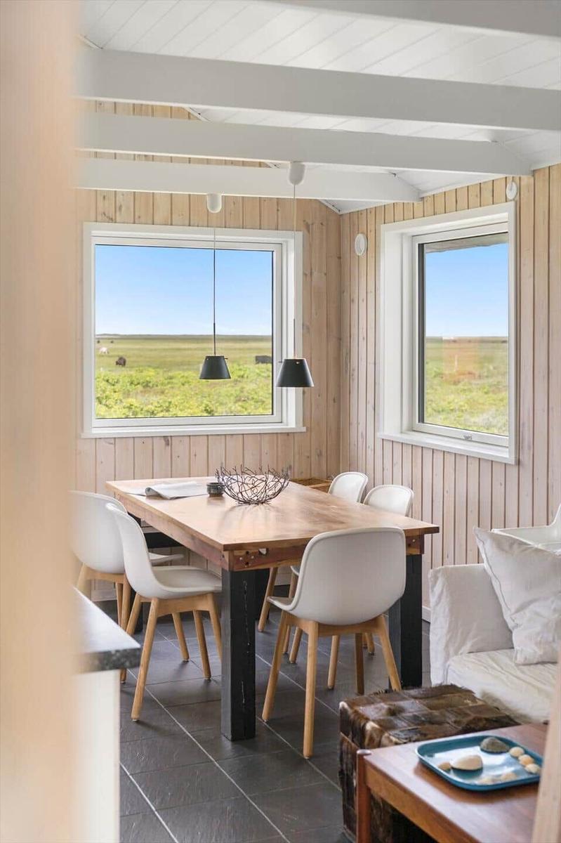 Esszimmer mit Holztisch, weißen Stühlen und Blick auf Felder.