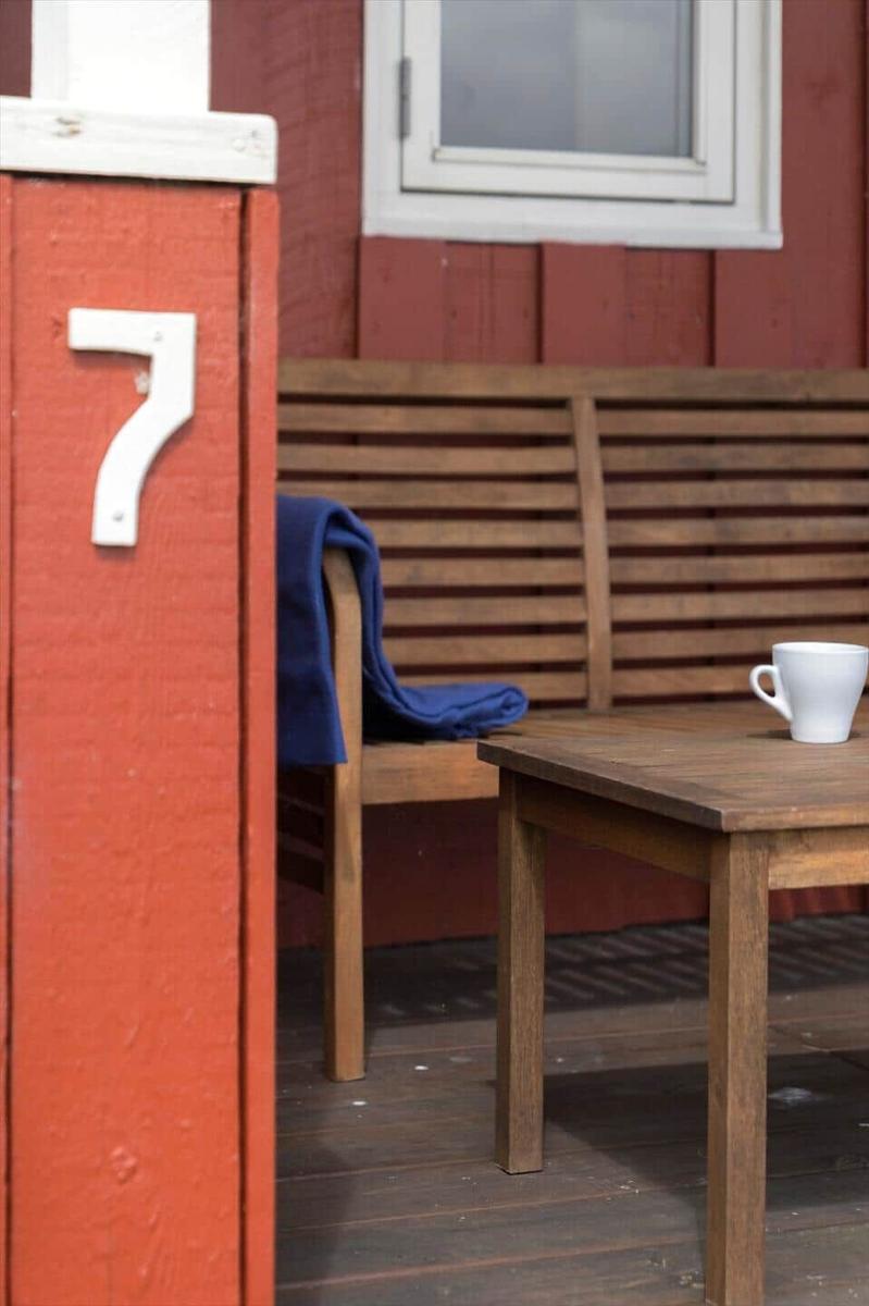 Hausnummer 7 an einer roten Wand. Holzbank, Tisch und Tasse auf der Terrasse.