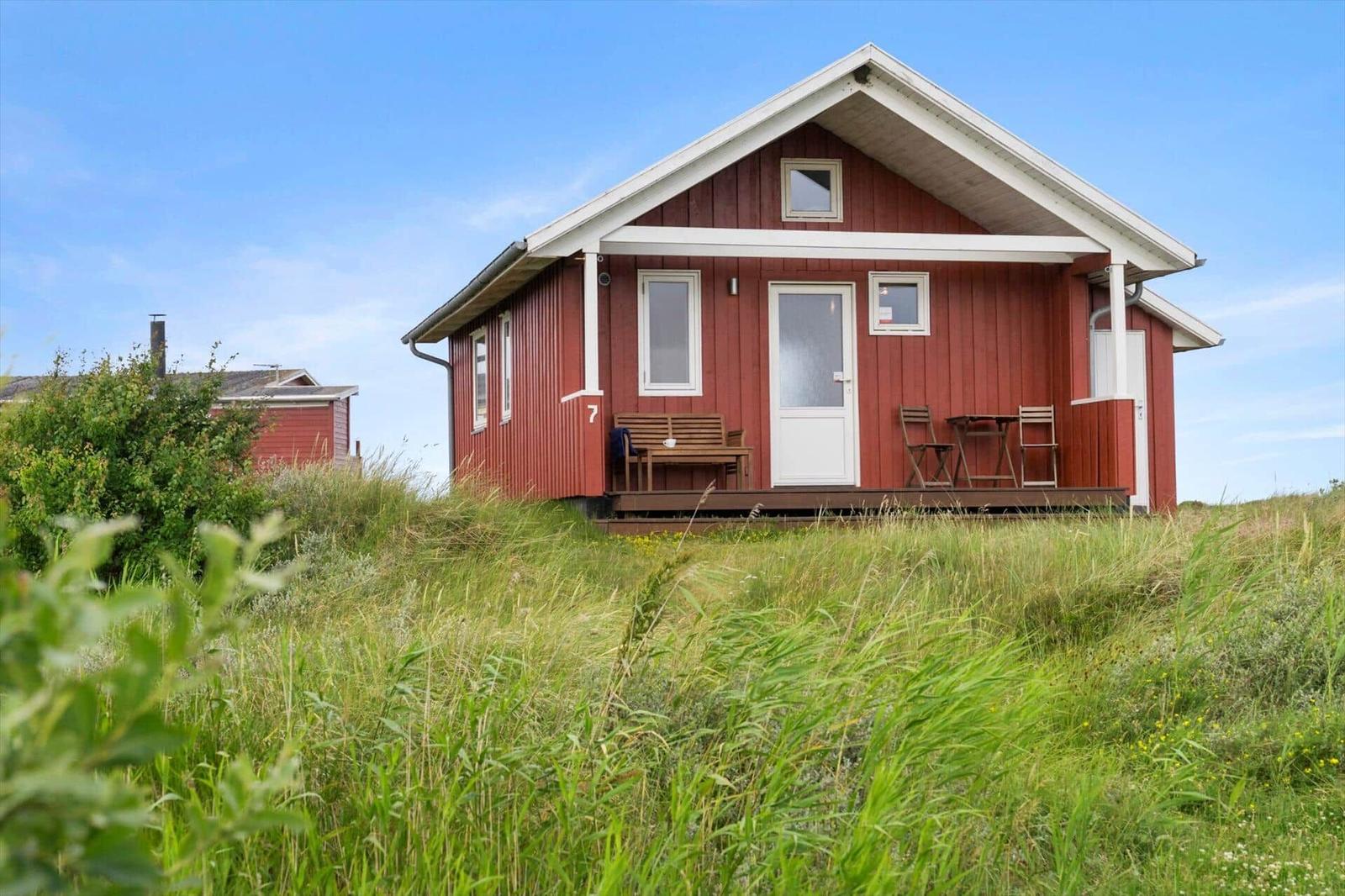 Rotes Holzhaus mit Terrasse und Garten. Tür und Fenster sind weiß.