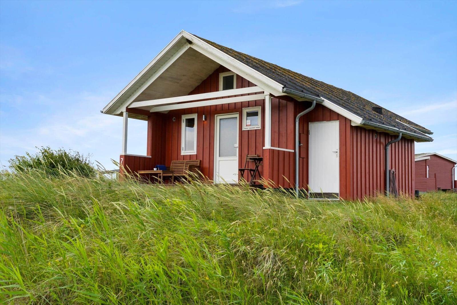Rotes Holzhaus mit weißer Tür und Veranda in Grasland.