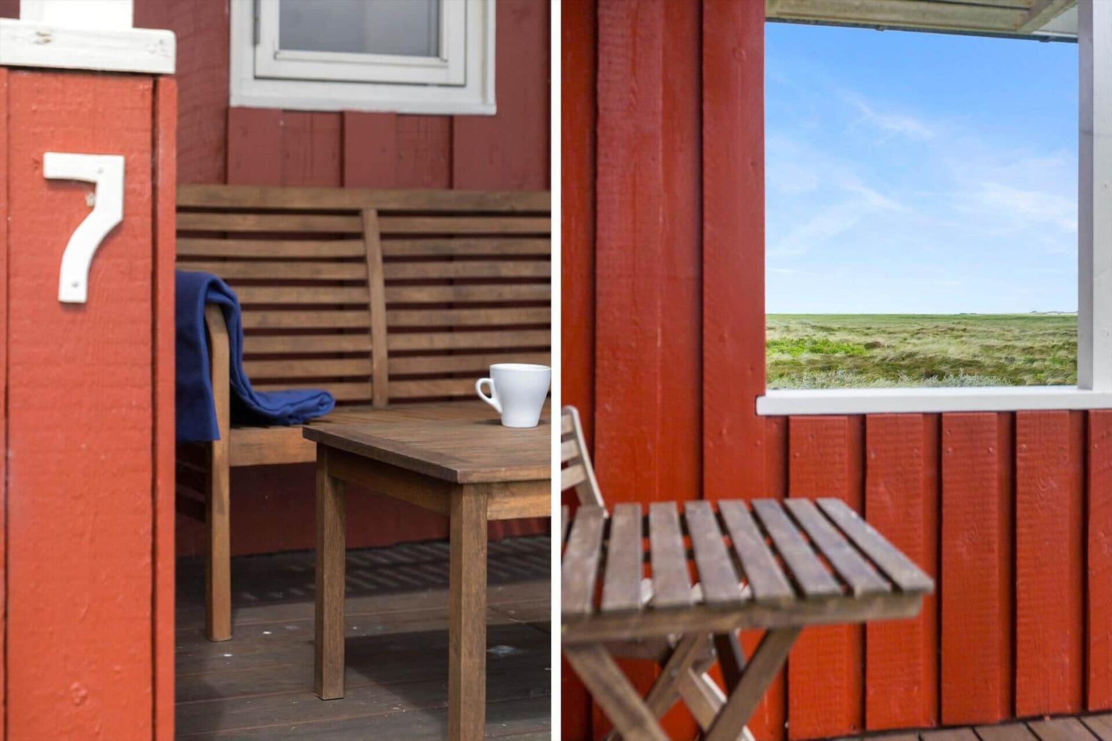 Roter Holzaufbau mit Tisch, Bank und Fensterblick auf Grasland.