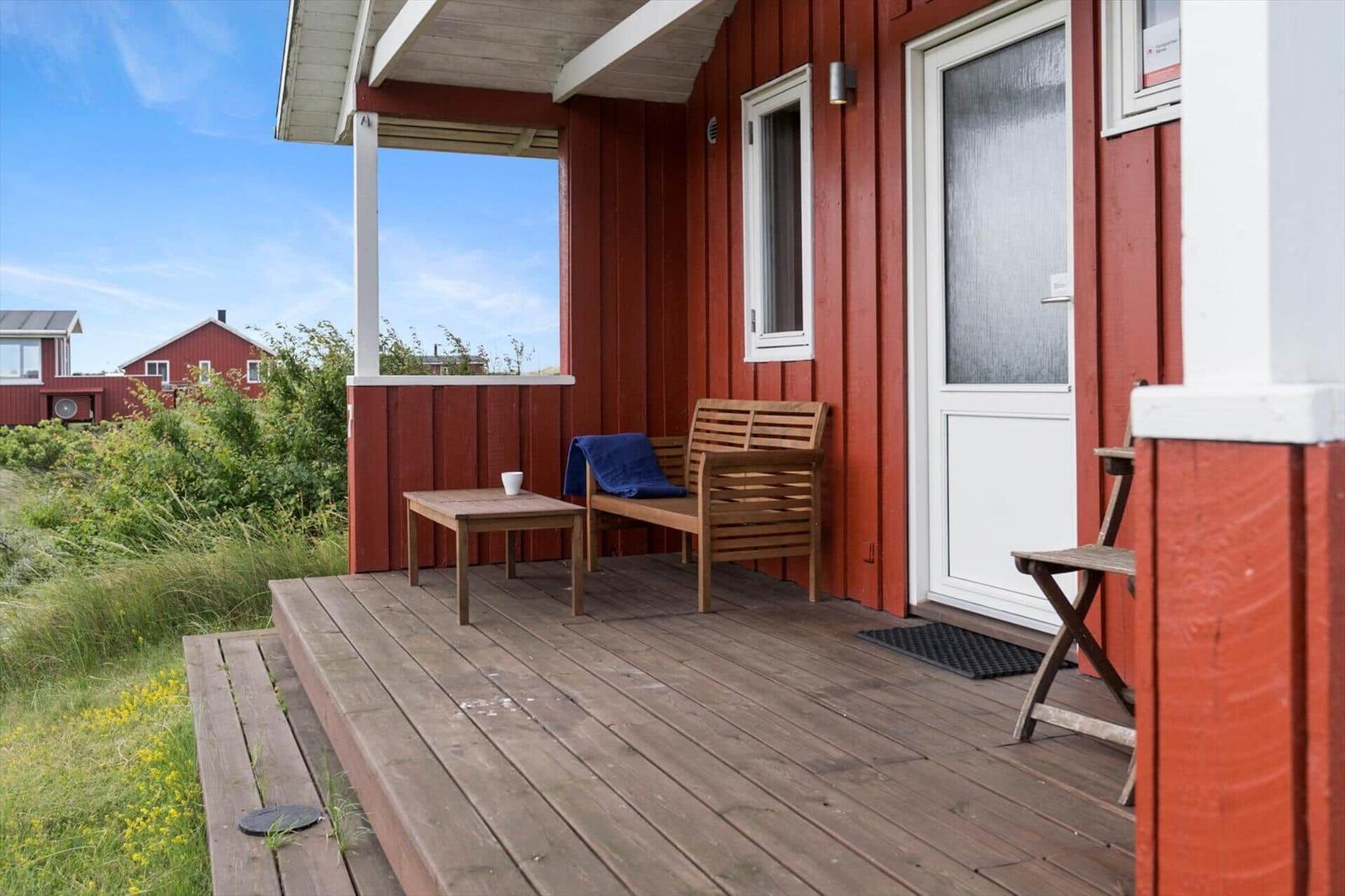 Holzterrasse mit Bank, Tisch und Tür an rotem Haus mit Blick auf Grasland.