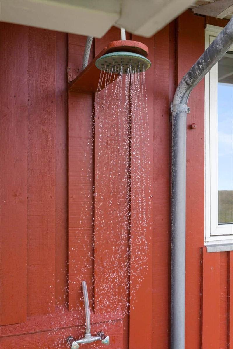 Außendusche an roter Holzwand mit laufendem Wasser