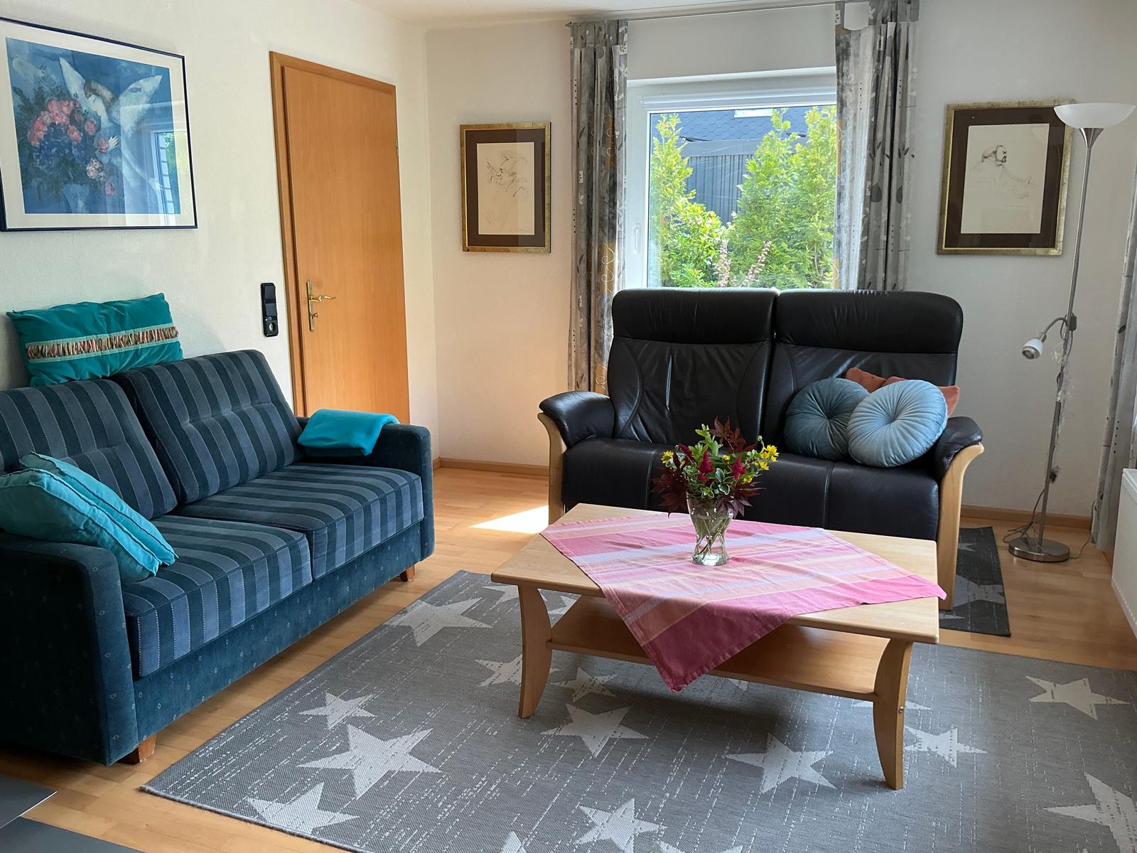 Wohnzimmer mit zwei Sofas, Tisch und Fenster. Auf dem Teppich sind Sterne zu sehen.