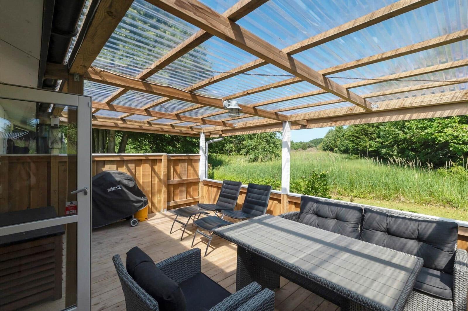 Terrasse mit Sitzgruppe unter Dach aus Holz und transparentem Material.