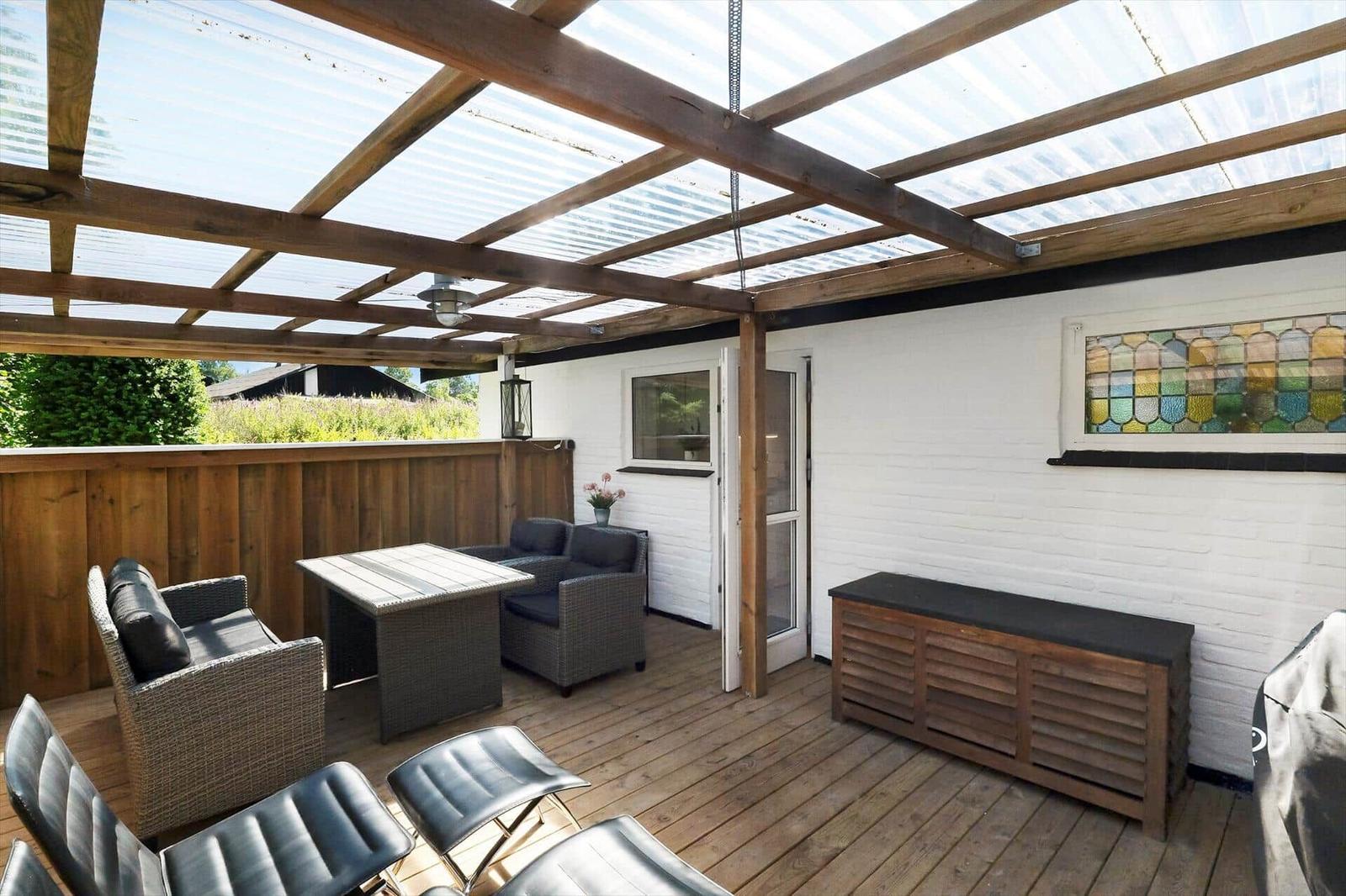 Terrasse mit Sitzgelegenheiten unter einer Holzkonstruktion mit Glasdach.