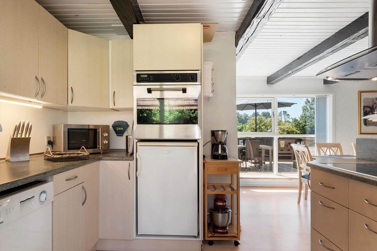 Küche mit Kühl- und Backofen, Arbeitsfläche und Blick auf Terrasse.