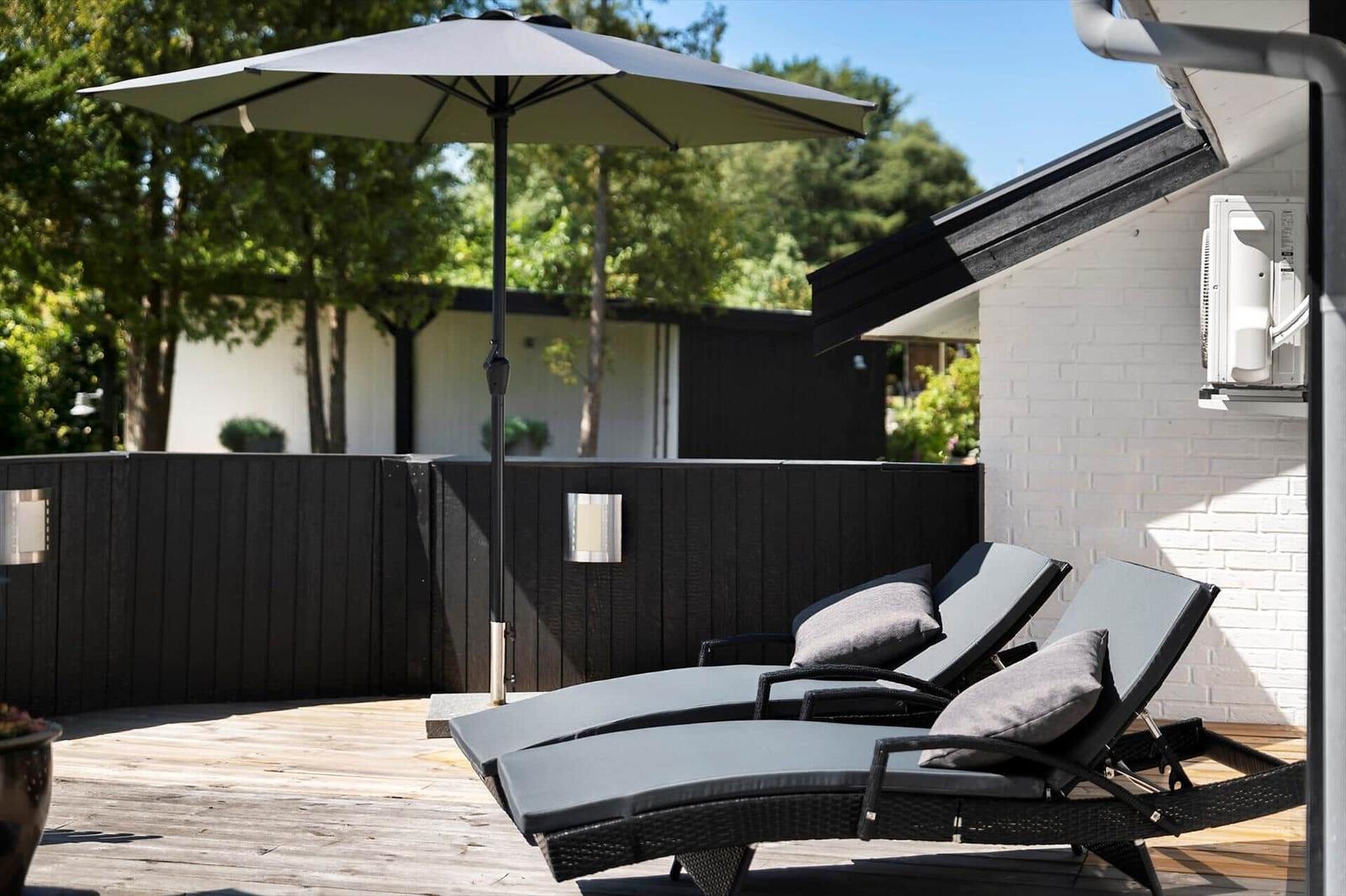 Terrasse mit zwei Liegen, Sonnenschirm und weißer Backsteinwand.