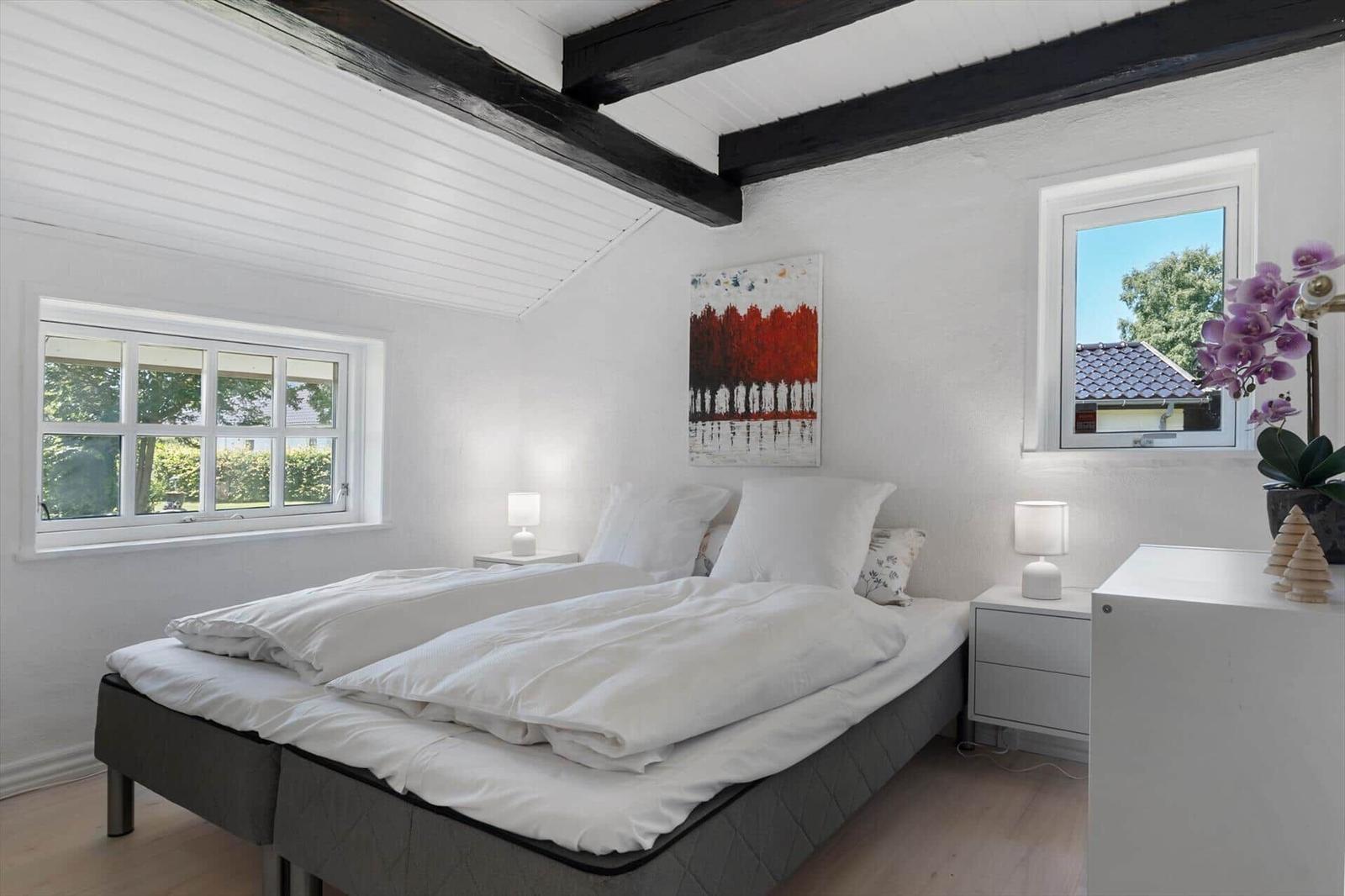 Schlafzimmer mit Doppelbett, zwei Fenstern und schwarzen Balken an der Decke.