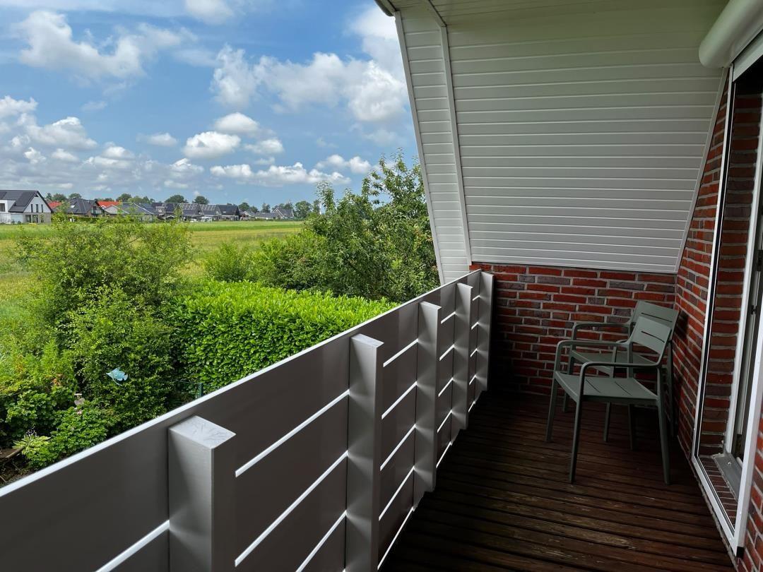 Terrasse mit Stühlen und Blick auf grüne Landschaft und Häuser.