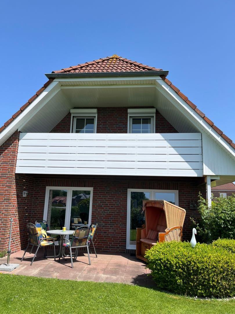 Haus mit Balkon, Terrasse und Gartenmöbel unter blauem Himmel.