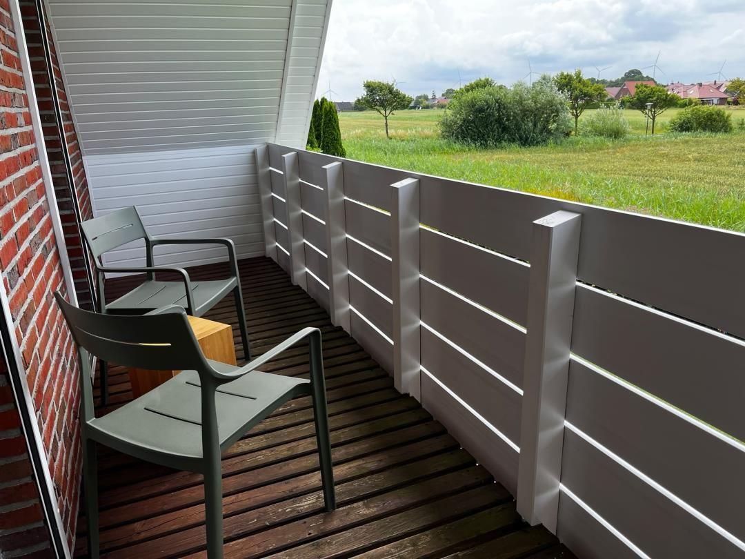 Terrasse mit zwei Stühlen und Tisch, Blick auf grünes Feld und Windräder.