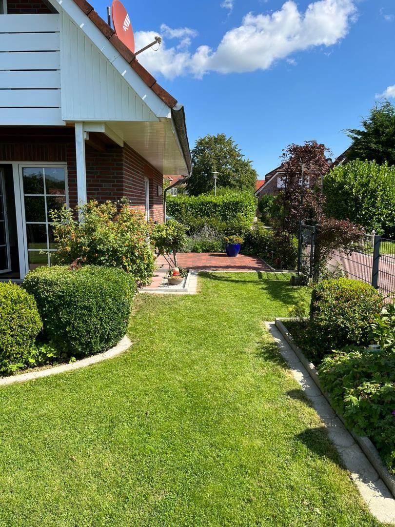 Grüner Rasenweg führt zum Haus mit Terrasse und gepflegtem Garten.