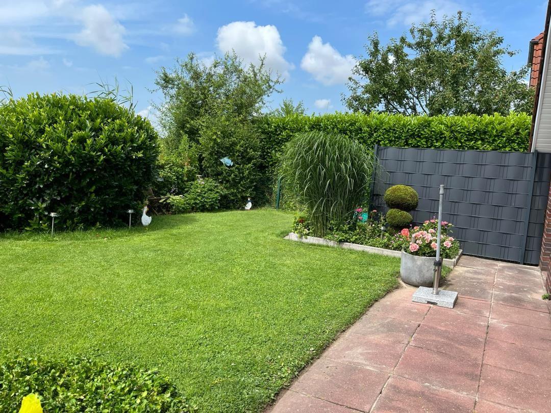 Garten mit Rasenfläche, Beete und Hecke. Terrasse aus roten Steinen.