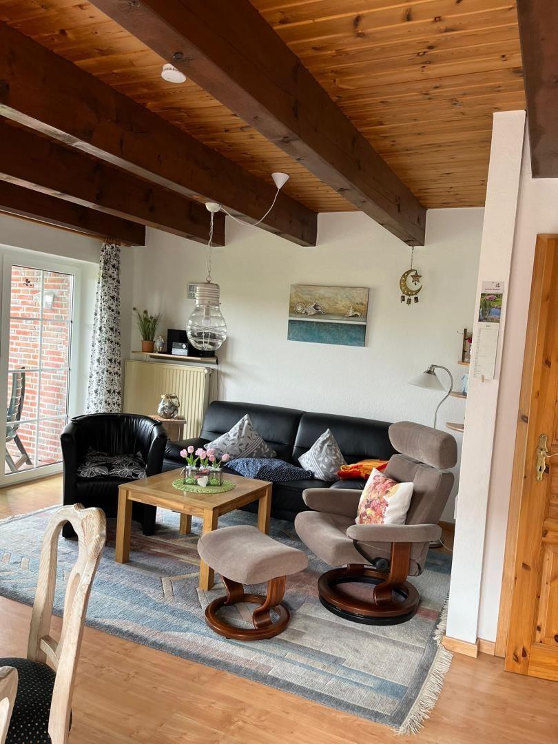 Wohnzimmer mit Holzbalkendecke, Sofa, Sessel und Couchtisch auf Teppich.