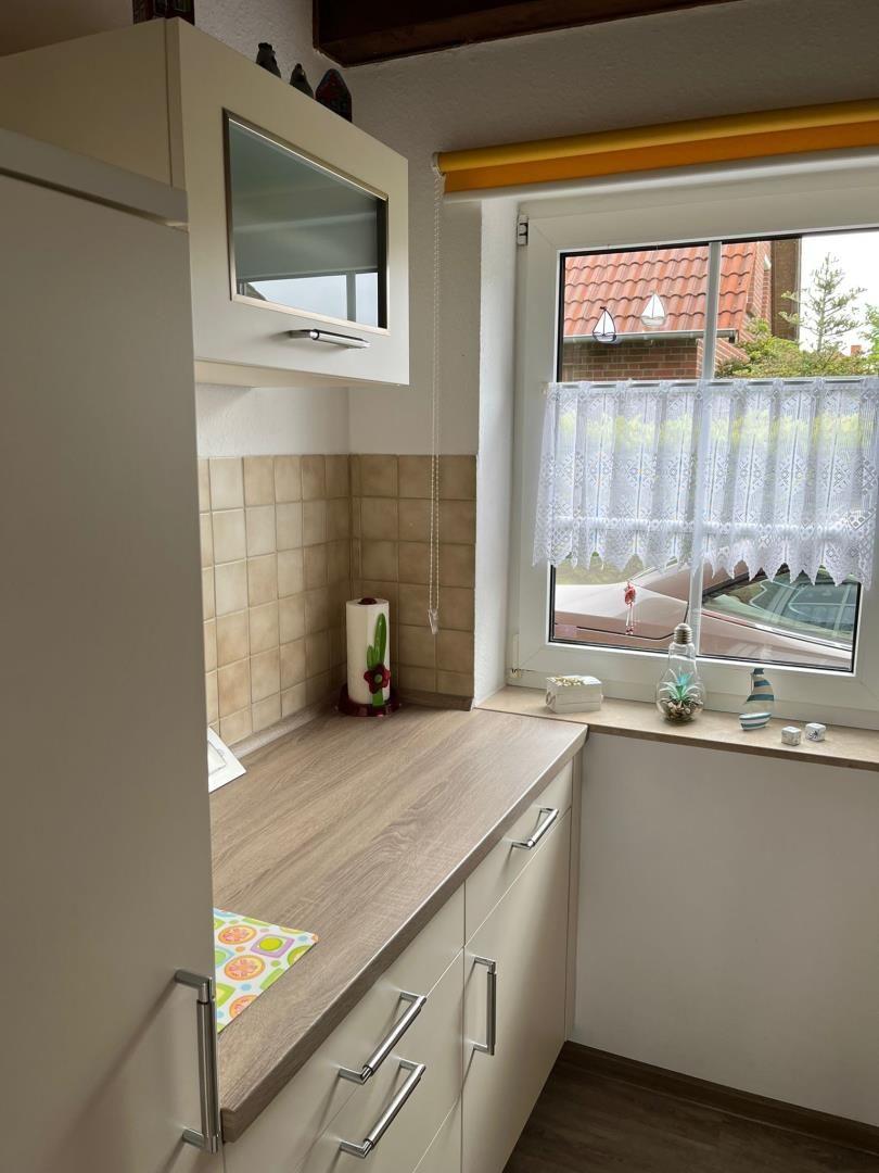 Küche mit Arbeitsplatte, Schränken und Fenster mit Vorhang.