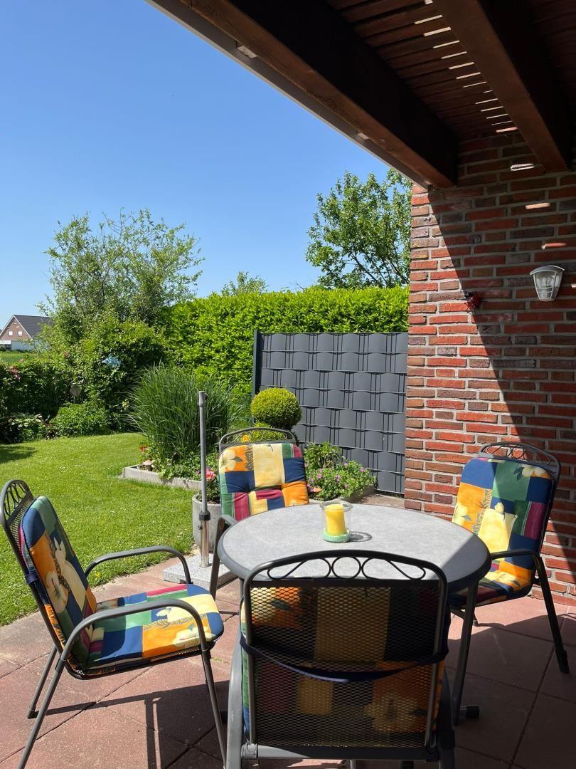 Terrasse mit Tisch und Stühlen, Blick auf grünen Garten und Ziegelwand.